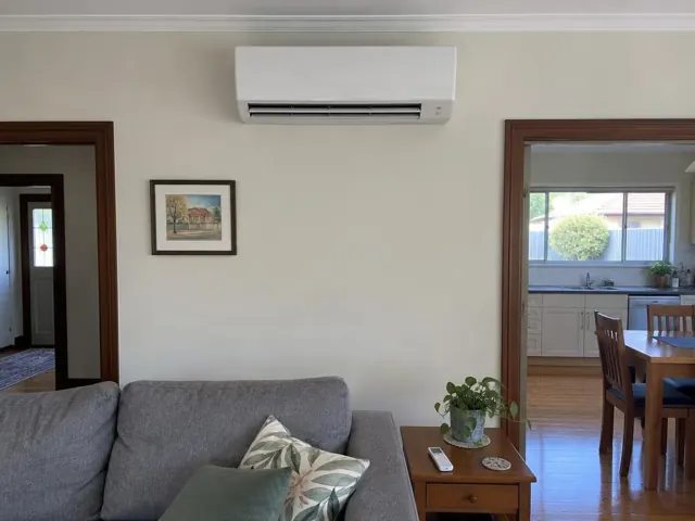 Wall-mounted split system above a living room opening into a kitchen, with cream walls and timber trim in Salisbury