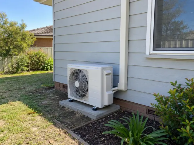 Outdoor air conditioner unit on a concrete pad beside a weatherboard house with pipe cover in Paralowie